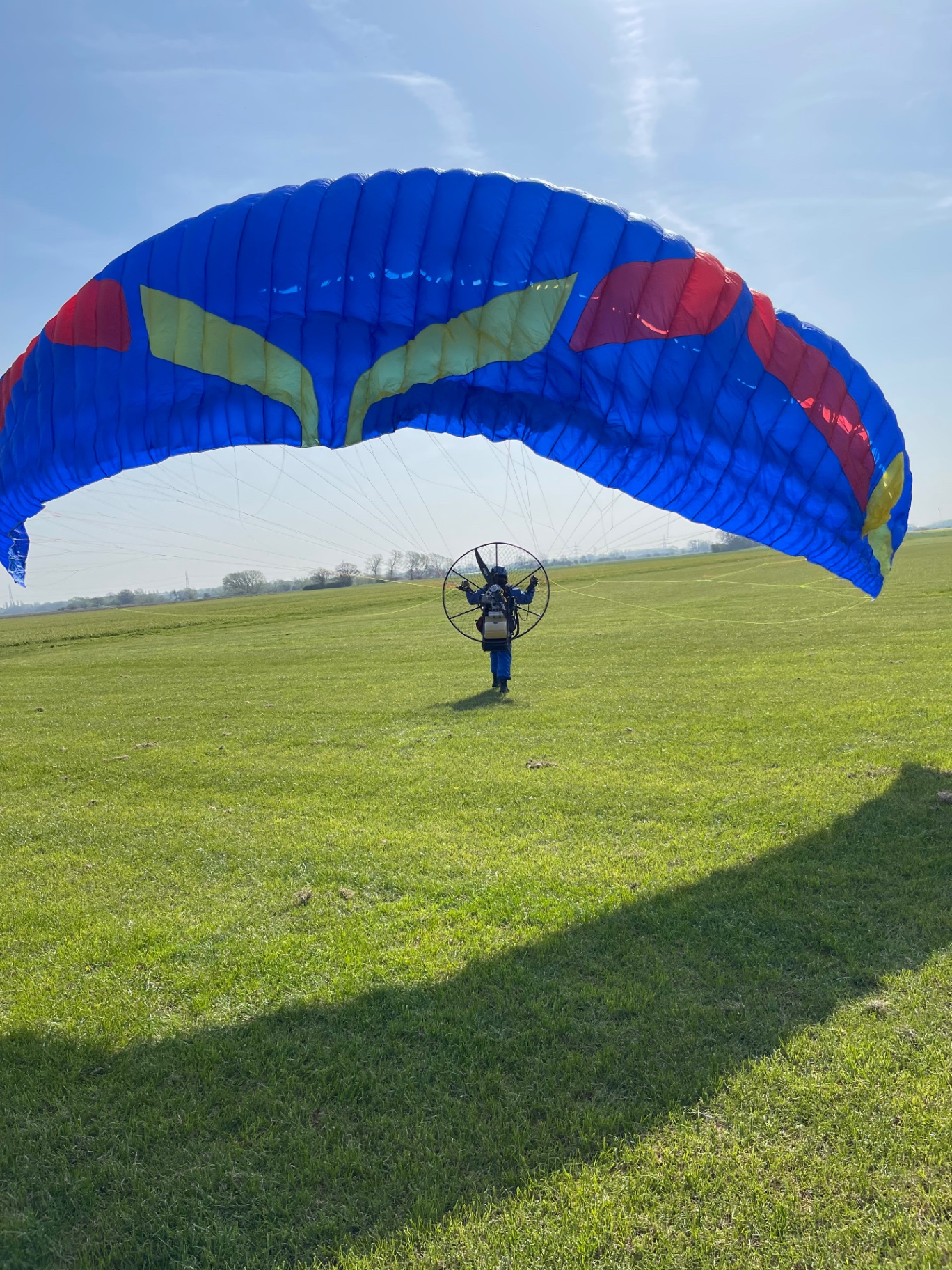 A paramotor pilot ground handling a blue wing on a grass airfield